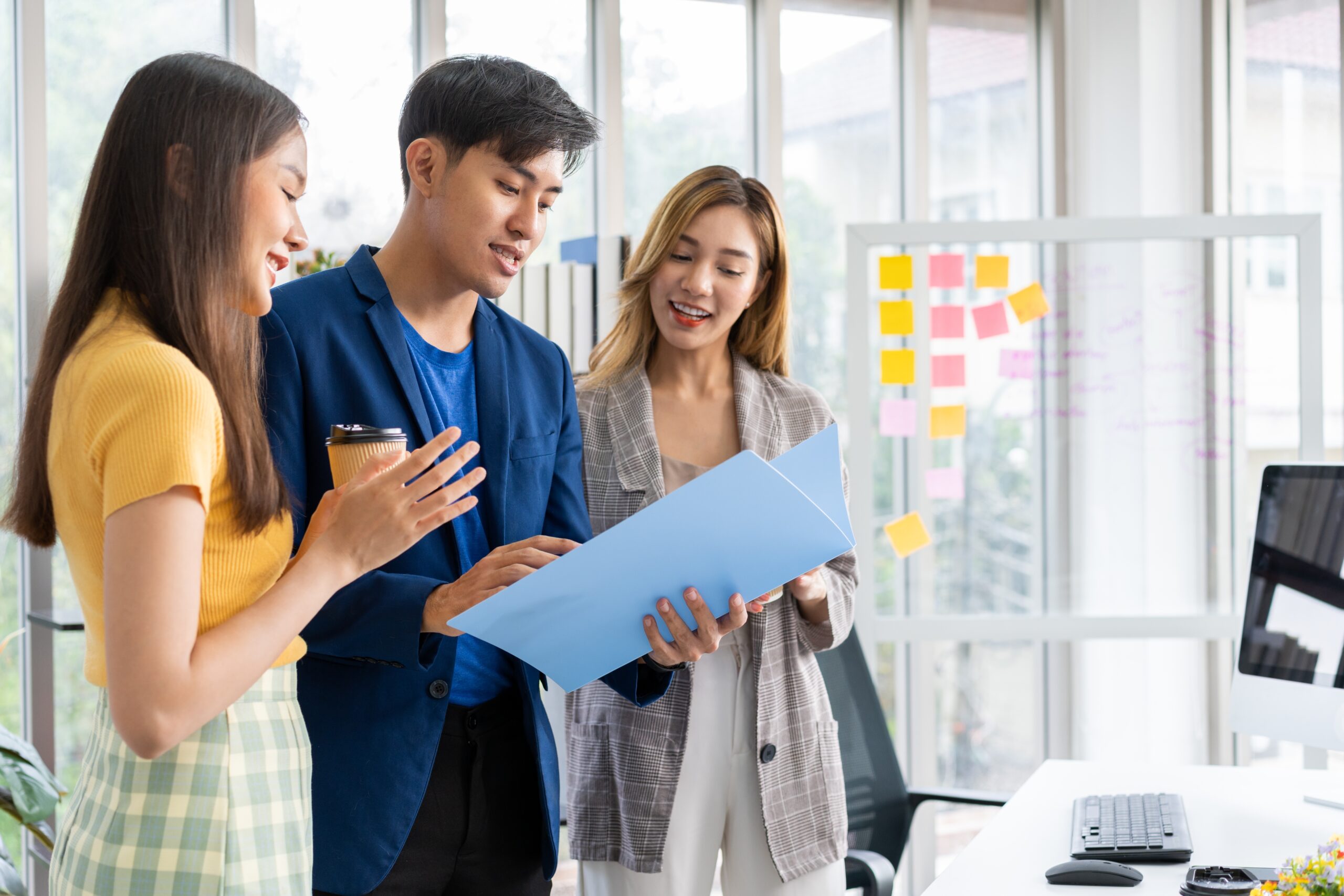 Three professionals collaborate in an office setting, reviewing documents while discussing ideas, with colorful sticky notes in the background.